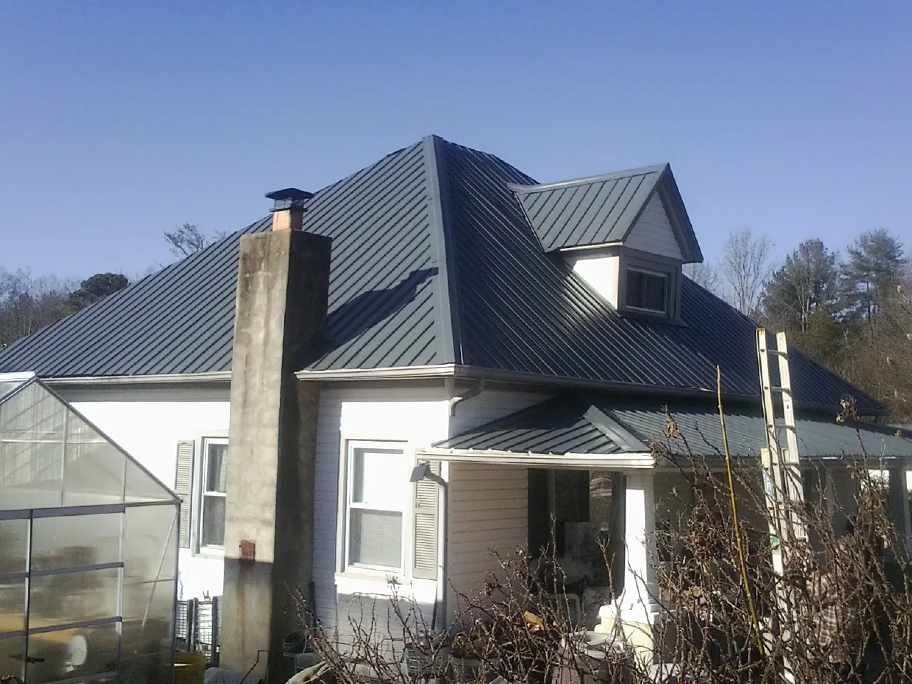 Dark blue standing seam metal roof on a white farmhouse with dormer — Slate & Tile Roof Repair by Roofing Brothers in Garland