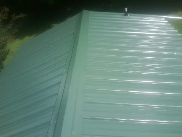 New green metal panels meeting at the ridge of a roof — Flat Roof Repair work by our crew in Garland