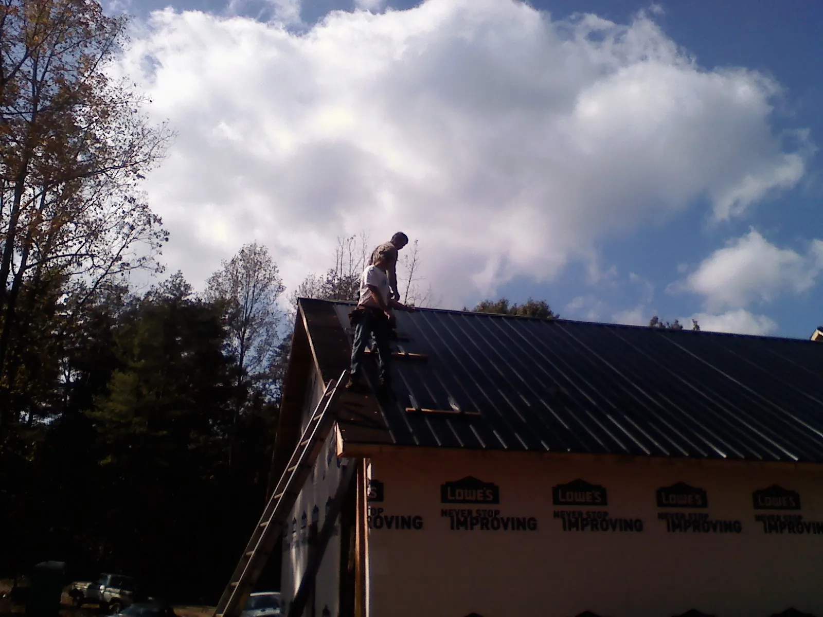 Roofer fastening dark metal panels high against a cloudy sky, from a Roof Inspection job in Garland
